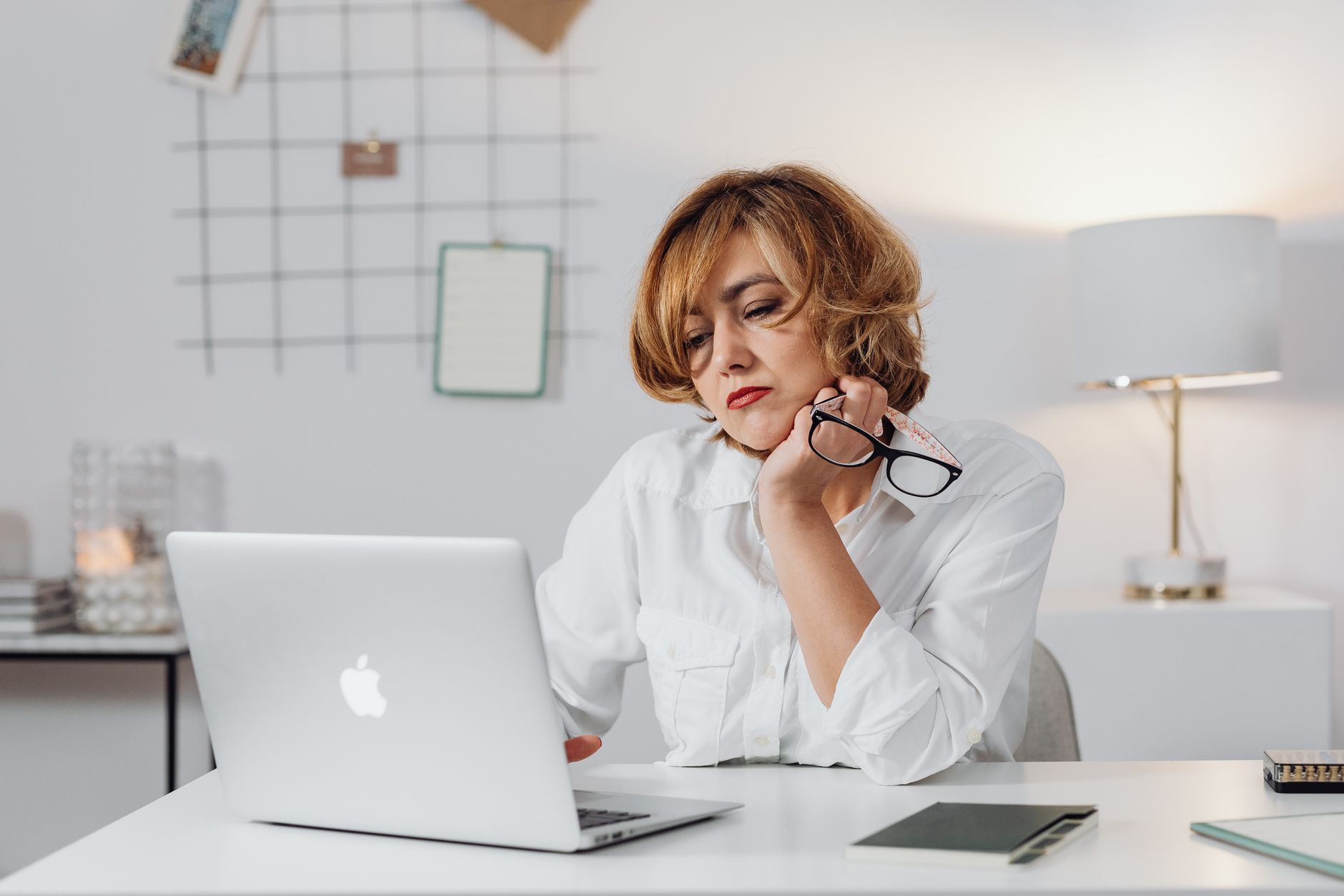 Woman holding her eyeglasses while reviewing something on her laptop